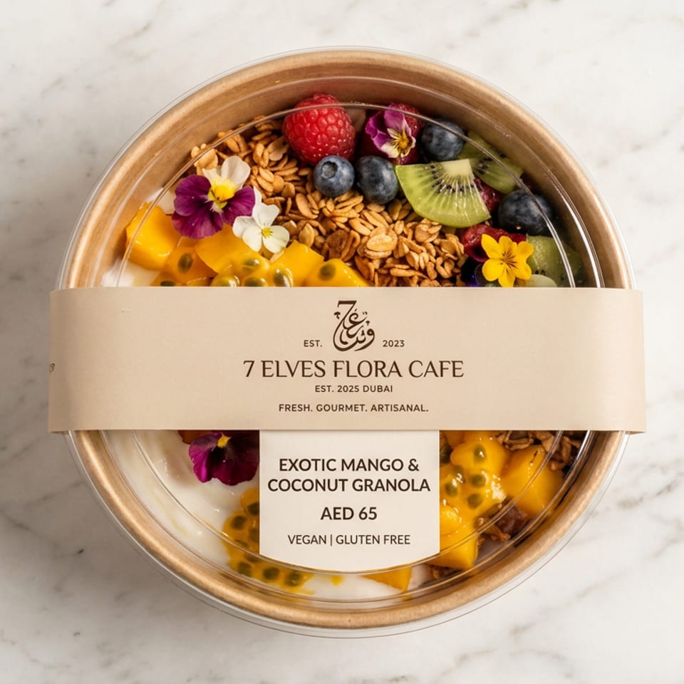 Packaged exotic mango and coconut granola bowl topped with fruit, edible flowers, and passion fruit on a marble surface.